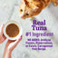 Hand holding bowl of tuna cat food with orange cat in background, promoting real tuna and natural ingredients.